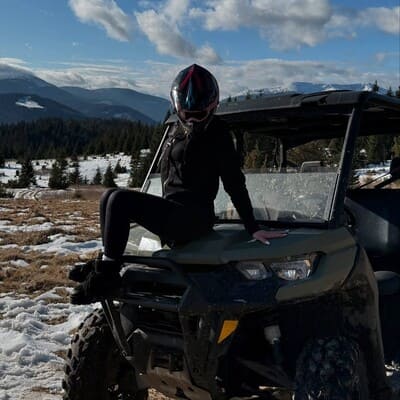 Дівчина в шоломі сидить на капоті багі на полонині в Карпатах, навесні, на фоні гірських вершин і залишків снігу