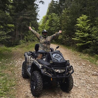 Людина стоїть на квадроциклі, піднявши руки догори на кам'яній дорозі в лісі Яремче, екстремальна поїздка в Карпатах