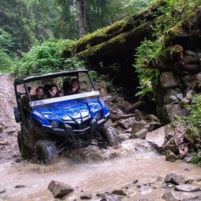 Двоє людей на синьому чотиримісному багі перетинають гірську річку під час дощу, екстремальна поїздка в Карпатах