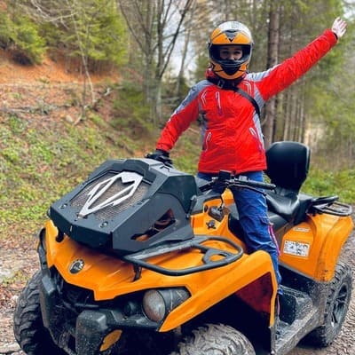 Людина стоїть на жовтому квадроциклі, піднявши одну руку догори в лісі Яремче, екстремальна поїздка на квадроциклі