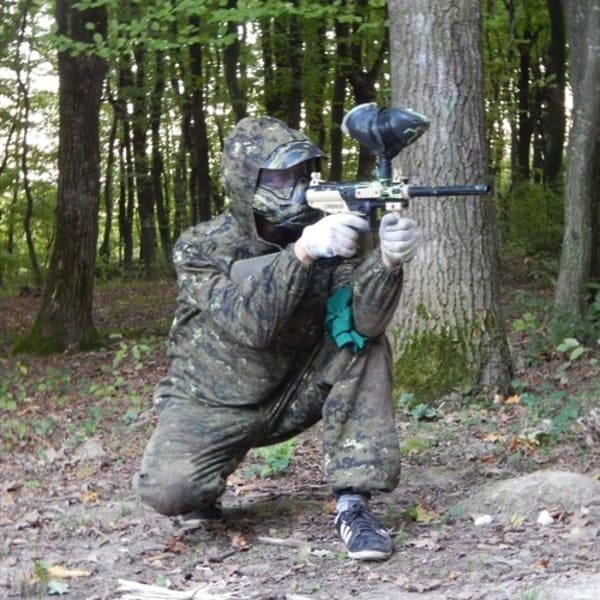 Гравець у пейнтбол у захисному спорядженні прицілюється з-за дерева в лісі