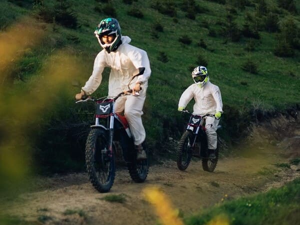 Дві людини на електробайках в білих костюмах їдуть стоячи гірською стежкою в Карпатах