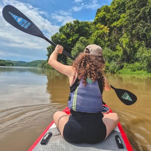 Дівчина на SUP-дошці гребе по Дністру, вигляд зі спини
