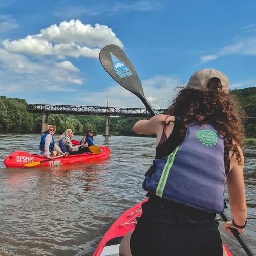Дівчина на SUP позаду каное з трьома дівчатами пливуть під міст, вигляд ззаду